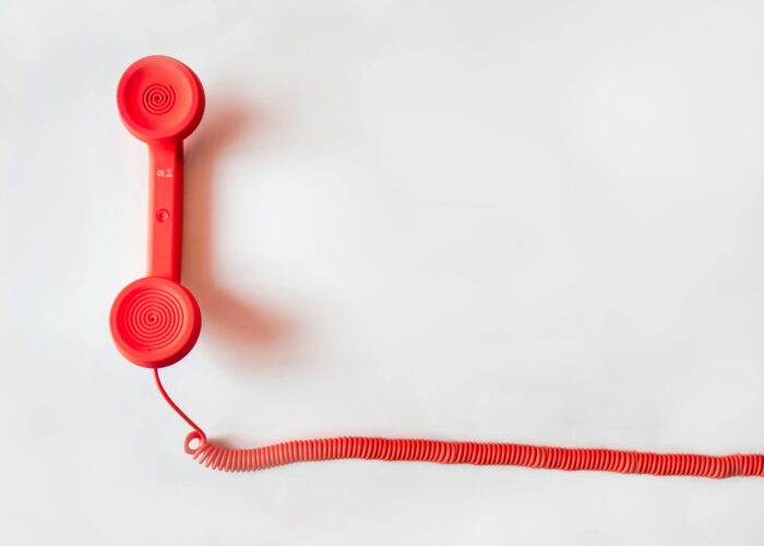 Vintage red phone handset with coiled cable on a clean white background, classic communication device.